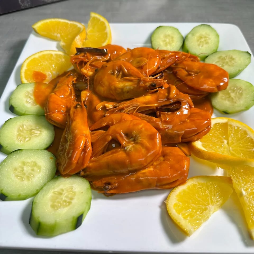A plate of orange-glazed Mexican shrimp, garnished with fresh cucumber slices and orange wedges.