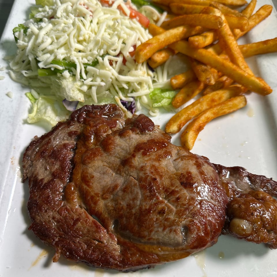Grilled steak with a side of french fries and a salad topped with shredded cheese.
