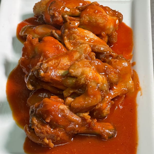 A white rectangular plate filled with chicken wings drenched in a vibrant orange-red sauce.