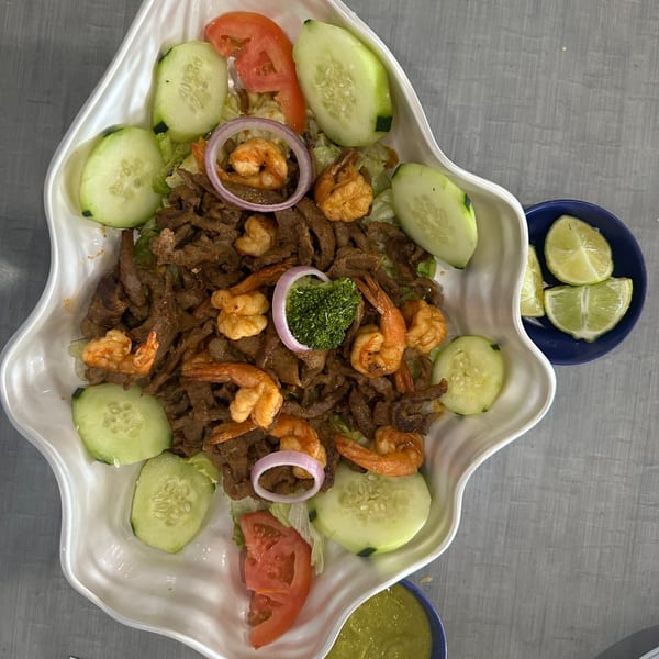 Mexican dish with shrimp, steak, cucumbers, tomatoes, and onions, served with lime and green sauce.